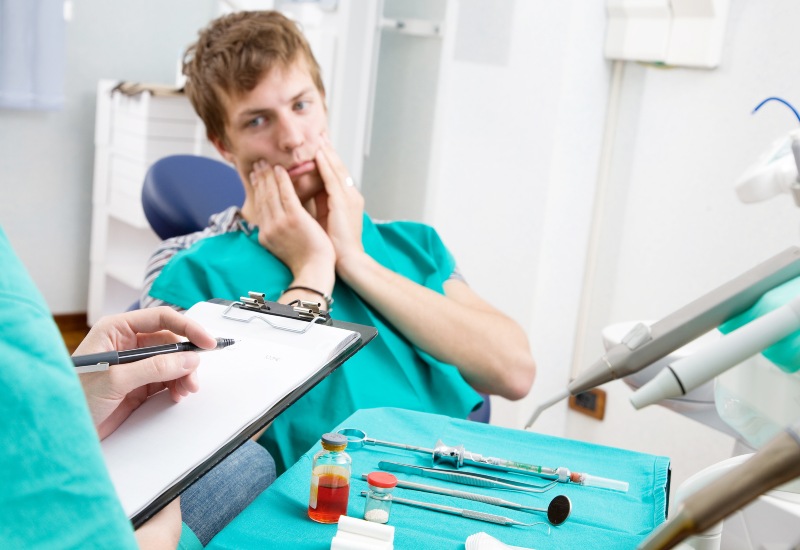 Patient covers face as dentist takes notes during emergency dental visit in Plainfield, IN